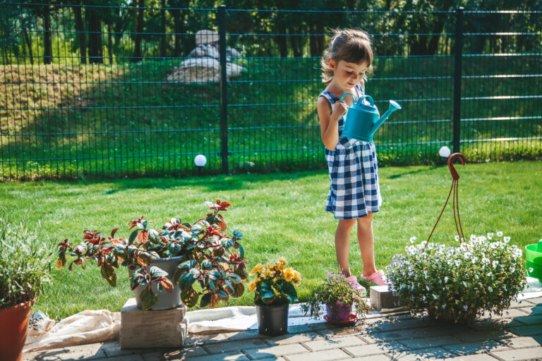 cute llittle girl 3 4 years old blue plaid dress watering plants from watering can garden kids having fun outside outdoor activity children